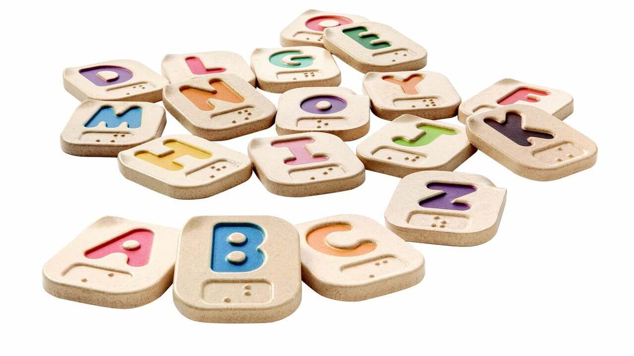 A photo of colorful Alphabet tiles with Braille underneath the letters on the tiiles