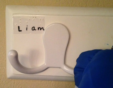 A white coat hook with a print and Braille label that reads "Liam"