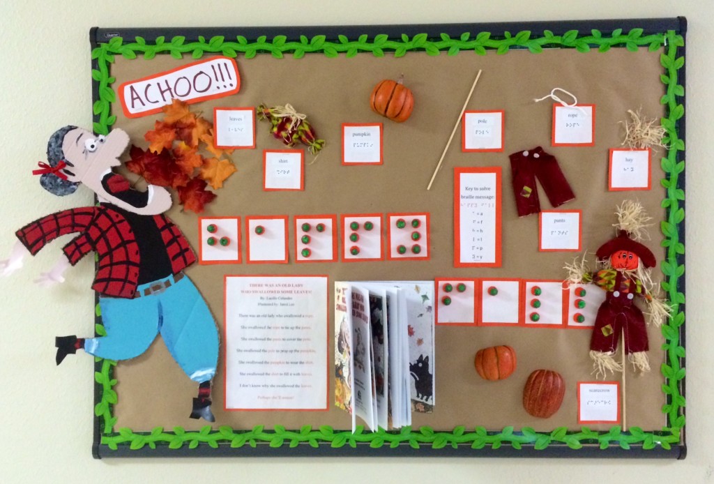 a bulletin board with Braille in the center. the boarder of the board is green. There is a sneezing person on the left, with surrounding feathers and a scarecrow.  